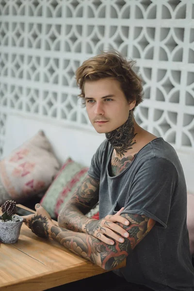 a tattooed man in a cafe uses a smartphone, drinks coffee, waiting for an order.