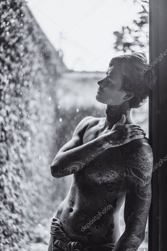 young tattooed man posing against the rain