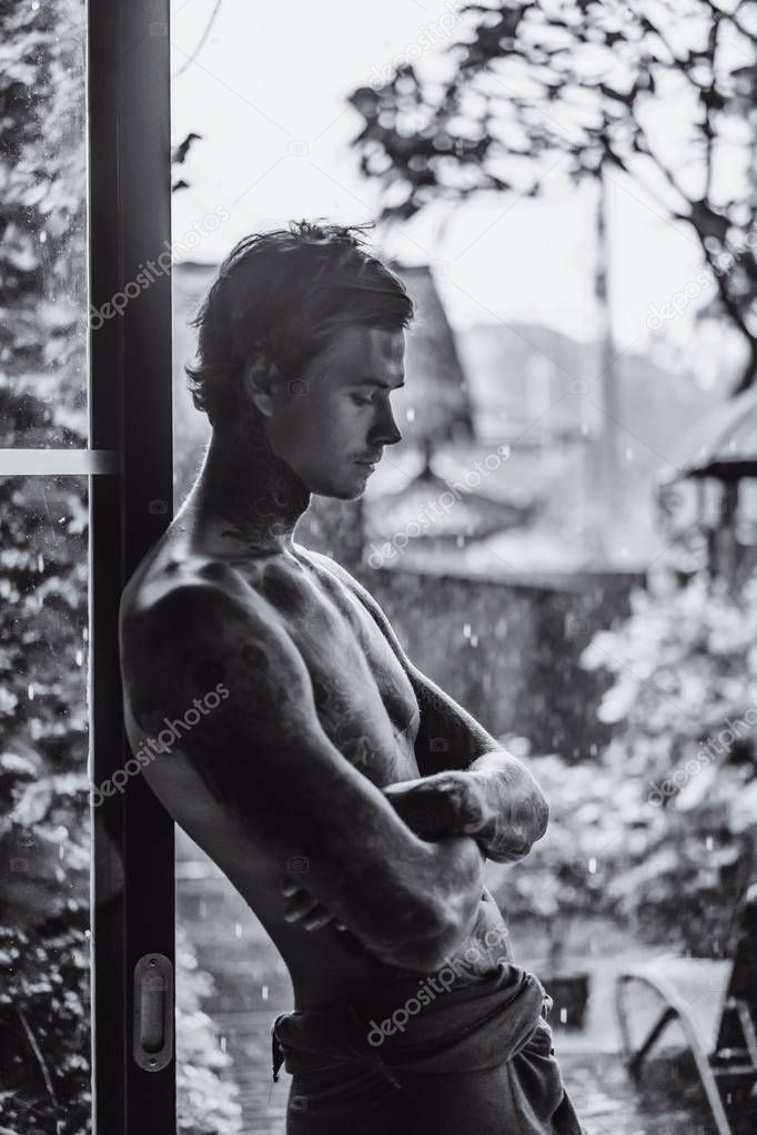 young tattooed man posing against the rain