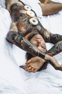 Genç, yakışıklı, dövmeli bir adam kahvaltısını yapıyor açık havada bahçede, açık havada, kahvaltıda çörek ve kahve içiyor..