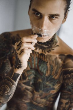 bir ayna, onun elinde bir tıraş jilet önünde genç bir yakışıklı dövmeli adam sabah tıraş.