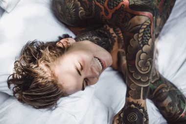 Dövmeli yakışıklı genç adam yatakta dinleniyor. 