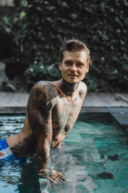 Açık Yüzme havuzunda dinlenme dövmeler genç yakışıklı adam. Dövmeli bir adam havuzda eğleniyor. Bali, Endonezya