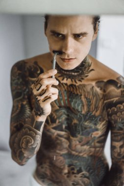 bir ayna, onun elinde bir tıraş jilet önünde genç bir yakışıklı dövmeli adam sabah tıraş.