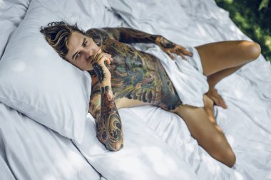 Dövmeli yakışıklı genç adam yatakta dinleniyor. 