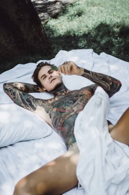Dövmeli yakışıklı genç adam yatakta dinleniyor. 