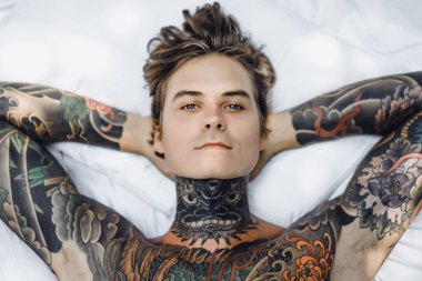 Dövmeli yakışıklı genç adam yatakta dinleniyor. 