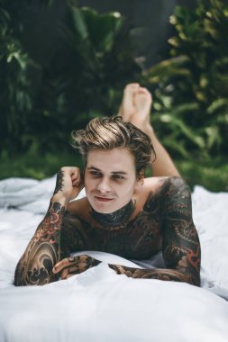 Dövmeli yakışıklı genç adam yatakta dinleniyor. 