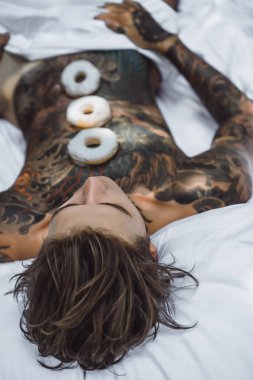 Genç, yakışıklı, dövmeli bir adam kahvaltısını yapıyor açık havada bahçede, açık havada, kahvaltıda çörek ve kahve içiyor..