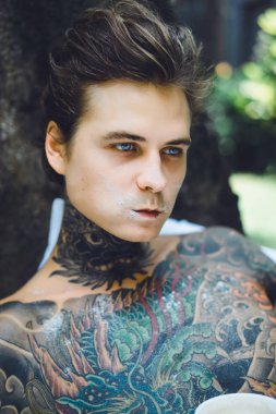 Genç, yakışıklı, dövmeli bir adam kahvaltısını yapıyor açık havada bahçede, açık havada, kahvaltıda çörek ve kahve içiyor..