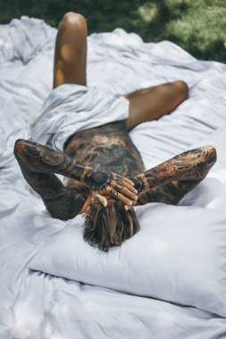 Dövmeli yakışıklı genç adam yatakta dinleniyor. 