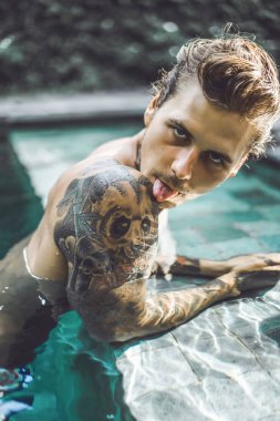 Açık Yüzme havuzunda dinlenme dövmeler genç yakışıklı adam. Dövmeli bir adam havuzda eğleniyor. Bali, Endonezya