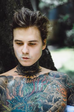 Genç, yakışıklı, dövmeli bir adam kahvaltısını yapıyor açık havada bahçede, açık havada, kahvaltıda çörek ve kahve içiyor..