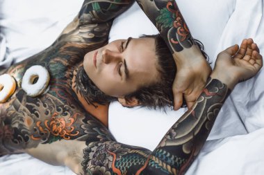 Genç, yakışıklı, dövmeli bir adam kahvaltısını yapıyor açık havada bahçede, açık havada, kahvaltıda çörek ve kahve içiyor..