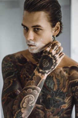 bir ayna, onun elinde bir tıraş jilet önünde genç bir yakışıklı dövmeli adam sabah tıraş.