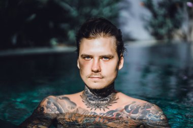 Açık Yüzme havuzunda dinlenme dövmeler genç yakışıklı adam. Dövmeli bir adam havuzda eğleniyor. Bali, Endonezya