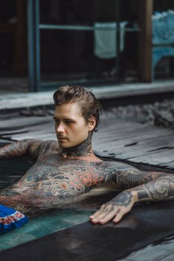 Açık Yüzme havuzunda dinlenme dövmeler genç yakışıklı adam. Dövmeli bir adam havuzda eğleniyor. Bali, Endonezya