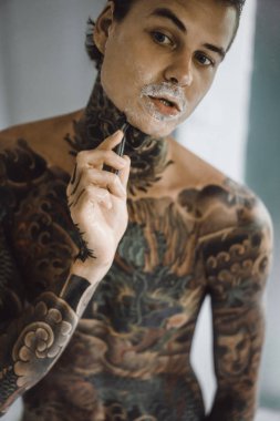 bir ayna, onun elinde bir tıraş jilet önünde genç bir yakışıklı dövmeli adam sabah tıraş.