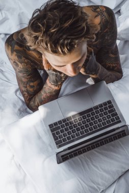 Yatakta dizüstü bilgisayarda çalışan, postaları kontrol eden, film izleyen, müzik dinleyen, Skype 'ta konuşan bir adam..