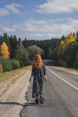 Uzun kızıl saçlı, keten elbiseli genç bir kadın. Ormanın arka planında doğal bir yerde..