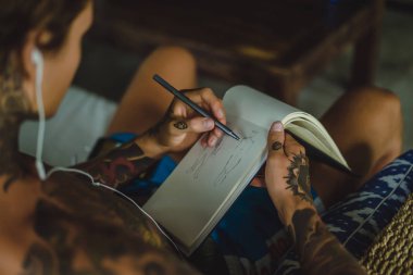 dövmeler kulaklıklar giyen genç bir erkekte müziği dinliyor ve içinde a defter bir kalem çizer. Çevrimiçi eğitim.