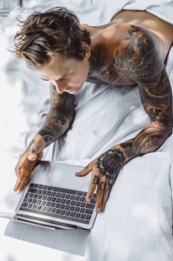 Yatakta dizüstü bilgisayarda çalışan, postaları kontrol eden, film izleyen, müzik dinleyen, Skype 'ta konuşan bir adam..