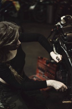 Garajda motosiklet tamir eden uzun saçlı güzel bir kız.