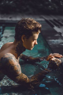 Açık Yüzme havuzunda dinlenme dövmeler genç yakışıklı adam. Dövmeli bir adam havuzda eğleniyor. Bali, Endonezya