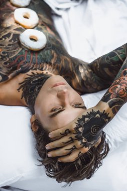 Genç, yakışıklı, dövmeli bir adam kahvaltısını yapıyor açık havada bahçede, açık havada, kahvaltıda çörek ve kahve içiyor..