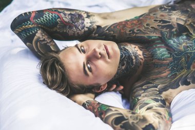 Dövmeli yakışıklı genç adam yatakta dinleniyor. 