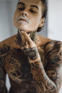 bir ayna, onun elinde bir tıraş jilet önünde genç bir yakışıklı dövmeli adam sabah tıraş.