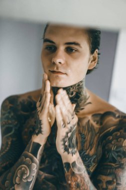 bir ayna, onun elinde bir tıraş jilet önünde genç bir yakışıklı dövmeli adam sabah tıraş.