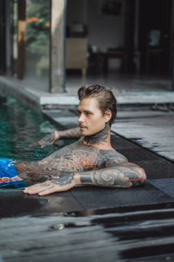 Açık Yüzme havuzunda dinlenme dövmeler genç yakışıklı adam. Dövmeli bir adam havuzda eğleniyor. Bali, Endonezya