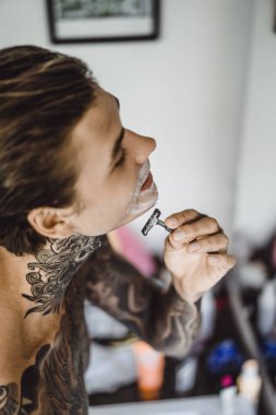 bir ayna, onun elinde bir tıraş jilet önünde genç bir yakışıklı dövmeli adam sabah tıraş.