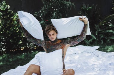 yakışıklı, Genç bir dövmeli adam sabah yatakta yastık fırlatır. Bahçe yatağında