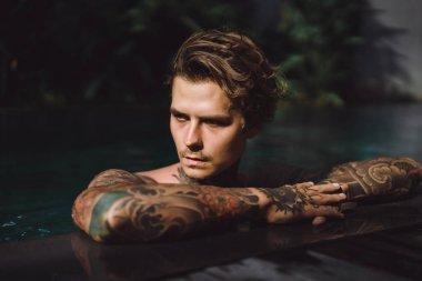 Açık Yüzme havuzunda dinlenme dövmeler genç yakışıklı adam. Dövmeli bir adam havuzda eğleniyor. Bali, Endonezya