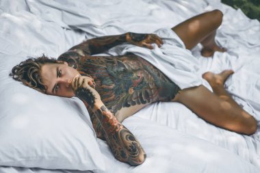 Dövmeli yakışıklı genç adam yatakta dinleniyor. 