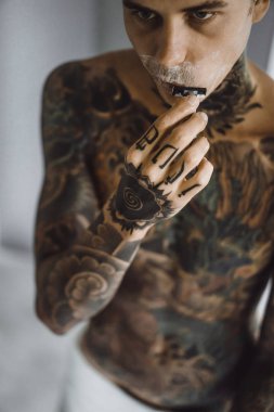 bir ayna, onun elinde bir tıraş jilet önünde genç bir yakışıklı dövmeli adam sabah tıraş.