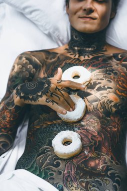 Genç, yakışıklı, dövmeli bir adam kahvaltısını yapıyor açık havada bahçede, açık havada, kahvaltıda çörek ve kahve içiyor..