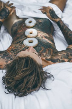 Genç, yakışıklı, dövmeli bir adam kahvaltısını yapıyor açık havada bahçede, açık havada, kahvaltıda çörek ve kahve içiyor..