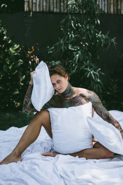 yakışıklı, Genç bir dövmeli adam sabah yatakta yastık fırlatır. Bahçe yatağında