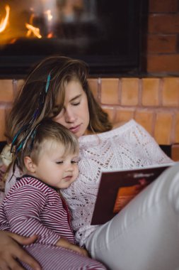 Genç anne ve oğlu şömine yakın bir masal kitabı mı okuyorsun.