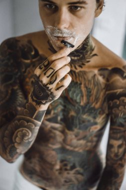 bir ayna, onun elinde bir tıraş jilet önünde genç bir yakışıklı dövmeli adam sabah tıraş.