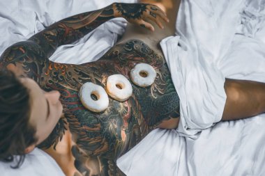 Genç, yakışıklı, dövmeli bir adam kahvaltısını yapıyor açık havada bahçede, açık havada, kahvaltıda çörek ve kahve içiyor..