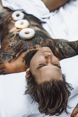 Genç, yakışıklı, dövmeli bir adam kahvaltısını yapıyor açık havada bahçede, açık havada, kahvaltıda çörek ve kahve içiyor..