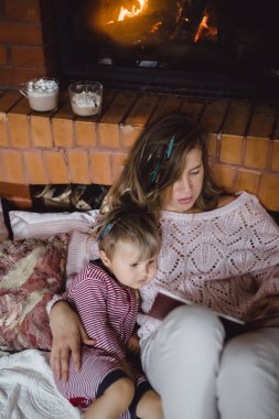 Genç anne ve oğlu şömine yakın bir masal kitabı mı okuyorsun.