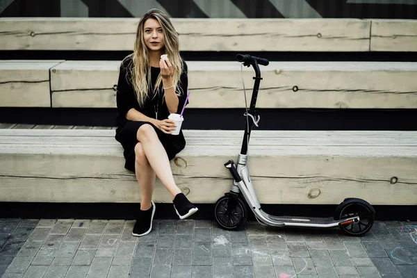 电单车上有长发的年轻女人 骑电动车的女孩喝咖啡 — 图库照片