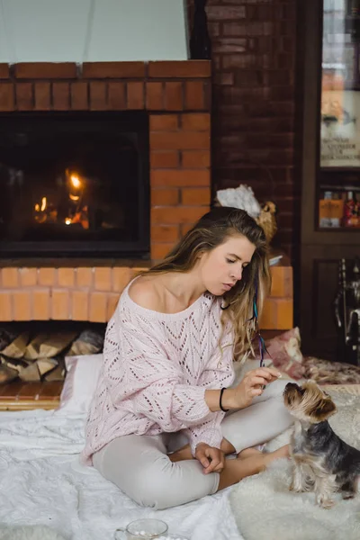 young woman with a dog near the fireplace drinks cocoa with marshmallows. Young beautiful girl with long hair is holding a york terrier