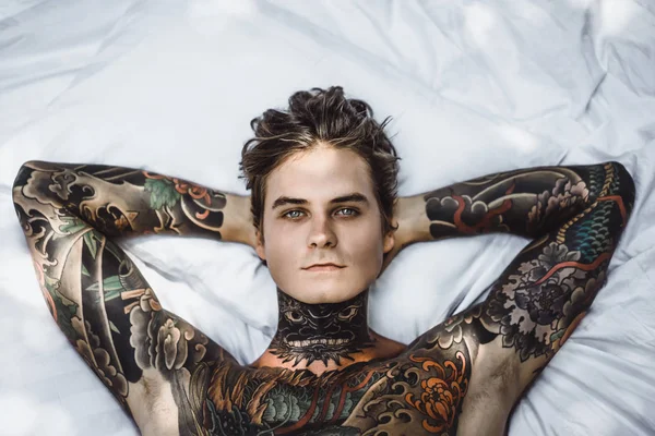 handsome young man in tattoos relaxing in bed