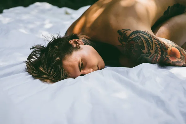 Молодой Красивый Татуированный Мужчина Утрам Постели Выбрасывает Подушки Кровать Саду — стоковое фото